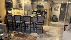 A modern kitchen with a central island, built-in appliances, and a dining area with chairs and a patterned rug. - Located right on the water! Modern 1-bedroom condo in tranquil Mismaloya  (Mismaloya)