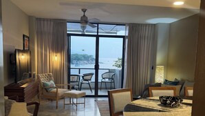 A spacious living area with a dining table, chairs, and a view of the sea through large windows. - Located right on the water! Modern 1-bedroom condo in tranquil Mismaloya  (Mismaloya)