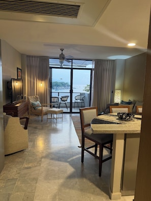 A spacious living area with a dining table, chairs, and a view of the sea through large windows. - Located right on the water! Modern 1-bedroom condo in tranquil Mismaloya  (Mismaloya)