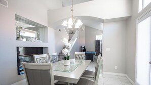 A dining area with a glass-top table, cushioned chairs, a chandelier, a fireplace, and a pool table. - Serene 5-bedrooms 3 bathrooms House with Pool in North Las Vegas (North Las Vegas)