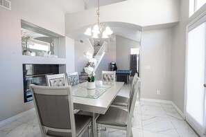 A dining area with a glass-top table, cushioned chairs, a chandelier, a fireplace, and a pool table. - Serene 5-bedrooms 3 bathrooms House with Pool in North Las Vegas (North Las Vegas)