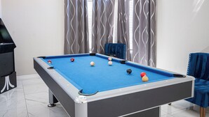 A pool table with balls, a blue chair, and a blue sofa in a room with a window and curtains. - Serene 5-bedrooms 3 bathrooms House with Pool in North Las Vegas (North Las Vegas)