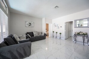 A spacious living room with a grey sectional sofa, a white tiled floor, and a door leading to another room. - Serene 5-bedrooms 3 bathrooms House with Pool in North Las Vegas (North Las Vegas)