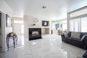 A spacious living room with a fireplace, a television mounted above it, and a dining area in the background. - Serene 5-bedrooms 3 bathrooms House with Pool in North Las Vegas (North Las Vegas)