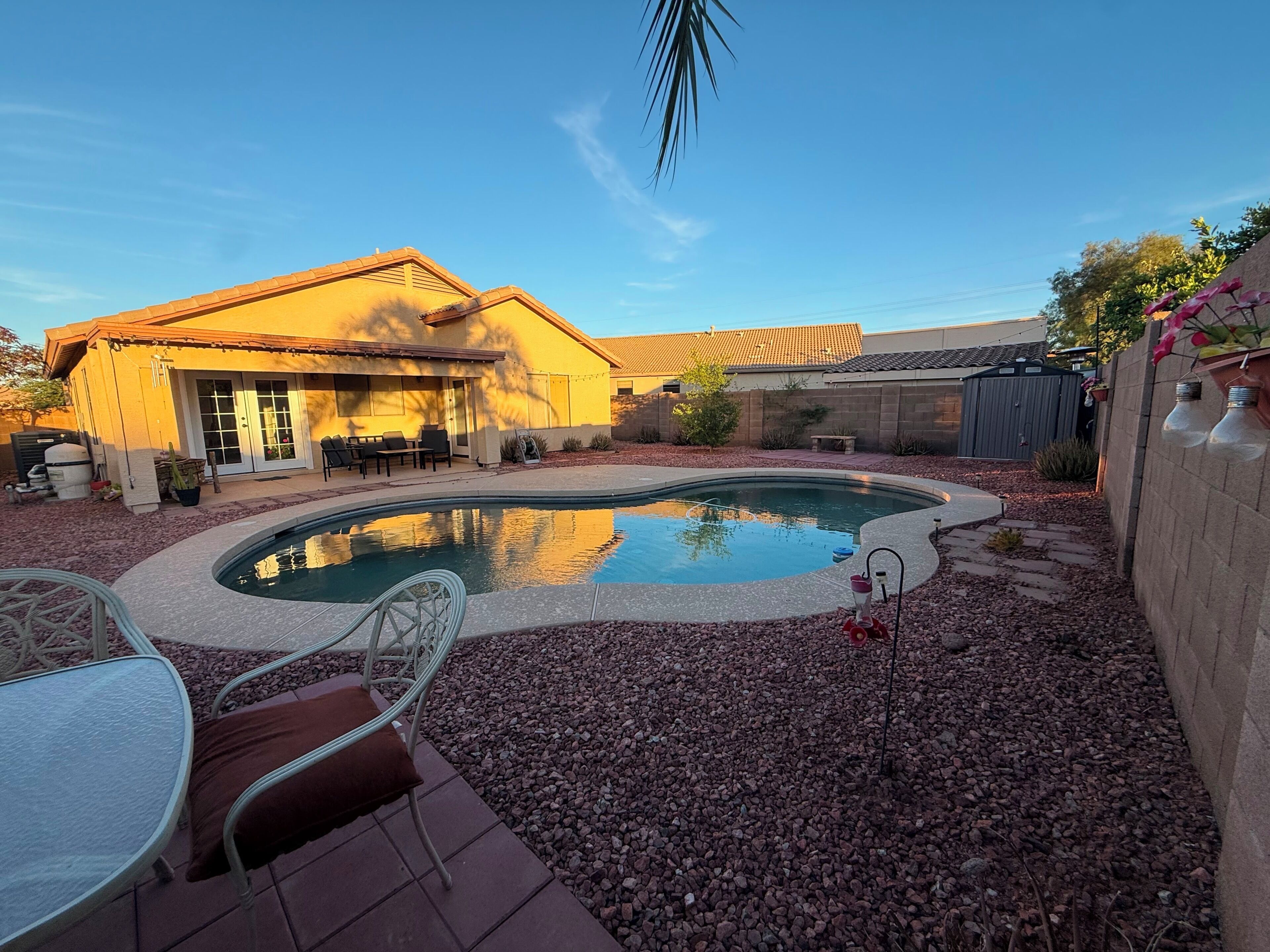 Un patio trasero residencial con piscina, mobiliario de jardín y una casa con techo de tejas.