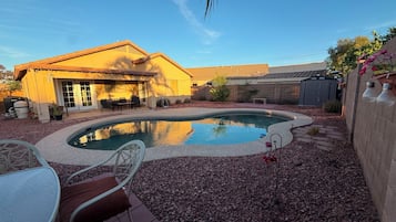 Un patio trasero residencial con piscina, mobiliario de jardín y una casa con techo de tejas.