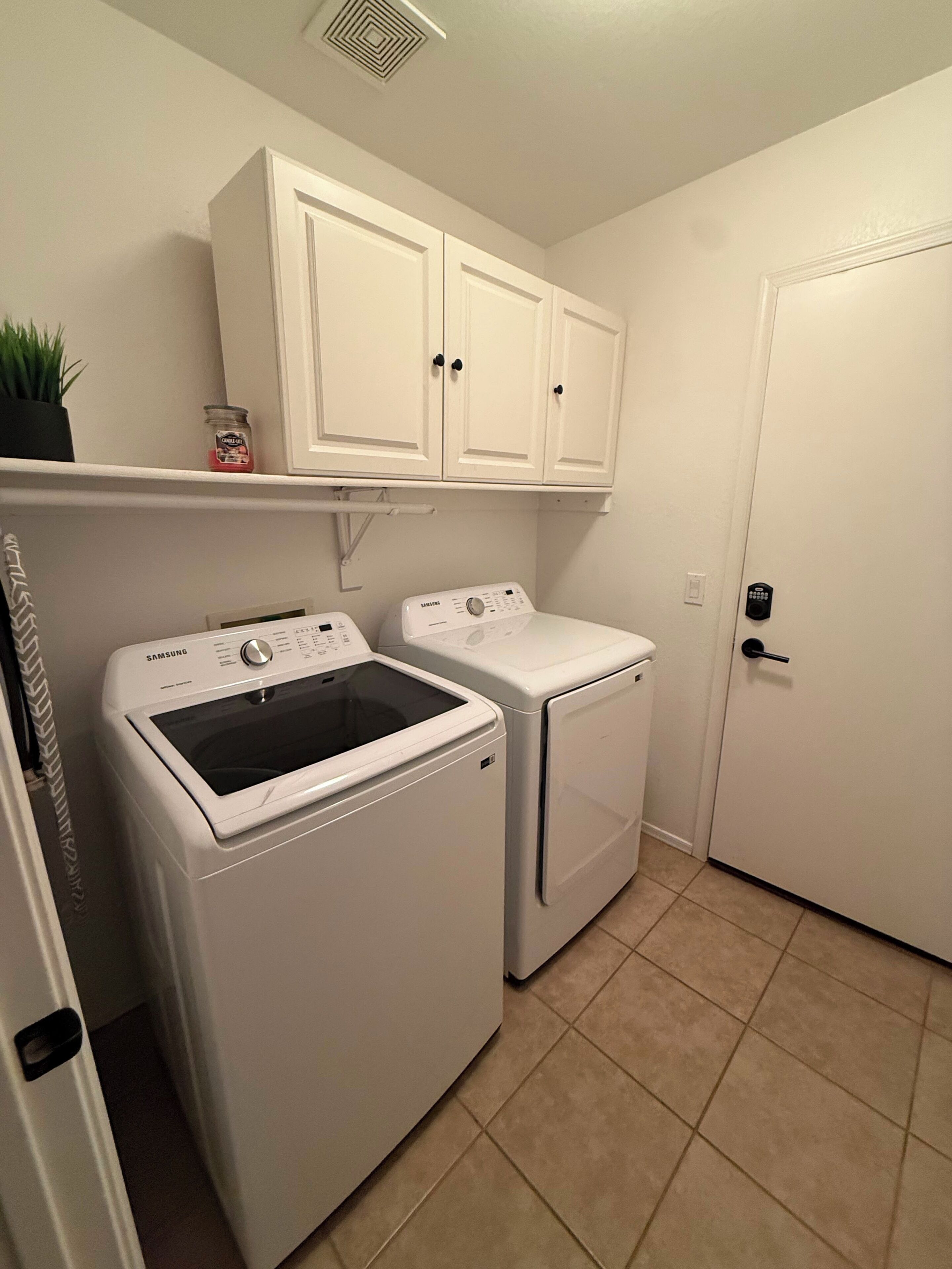 A laundry room with two white washing machines, a cabinet above, and a door to the right.