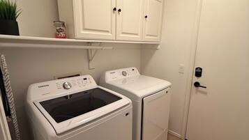 A laundry room with two white washing machines, a cabinet above, and a door to the right.