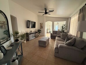 A living room with a sofa, ottoman, TV, and a ceiling fan.