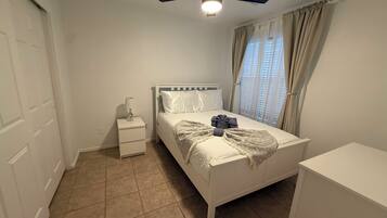 A bedroom with a bed, a nightstand, a ceiling fan, and a window with curtains.