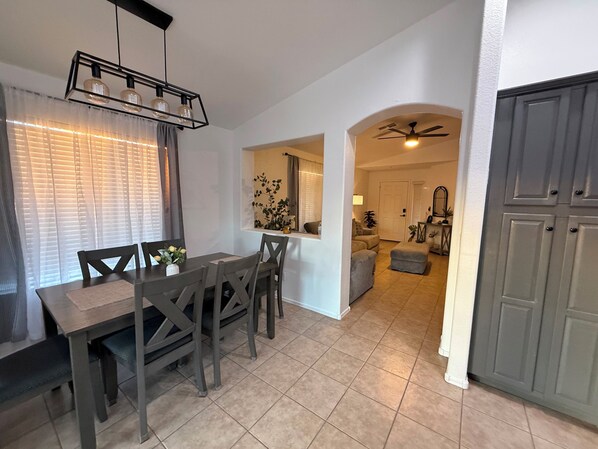 A dining area with a table and chairs, a ceiling fan, and a view into the living room.