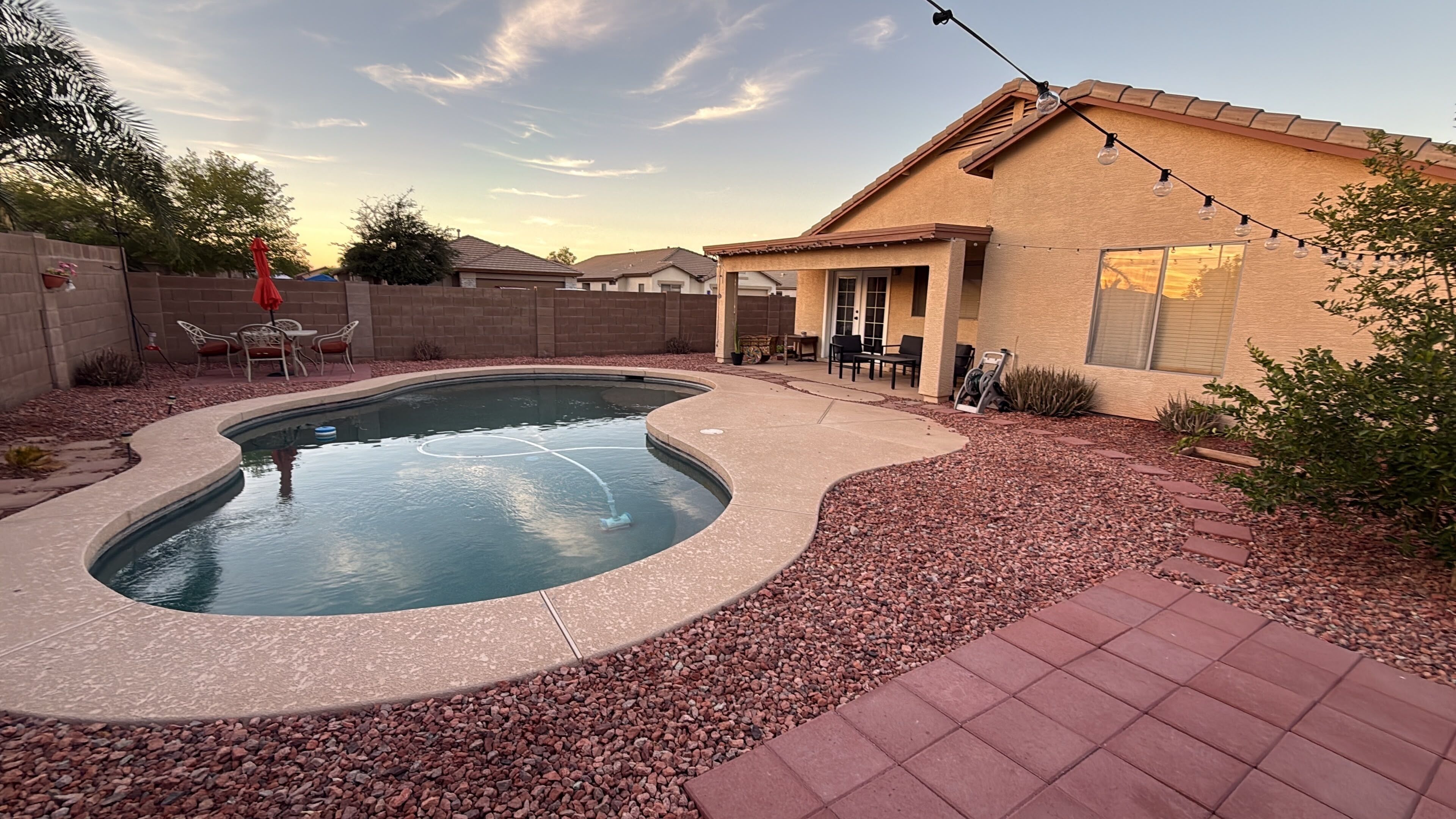 A backyard with a swimming pool, patio furniture, and a house.
