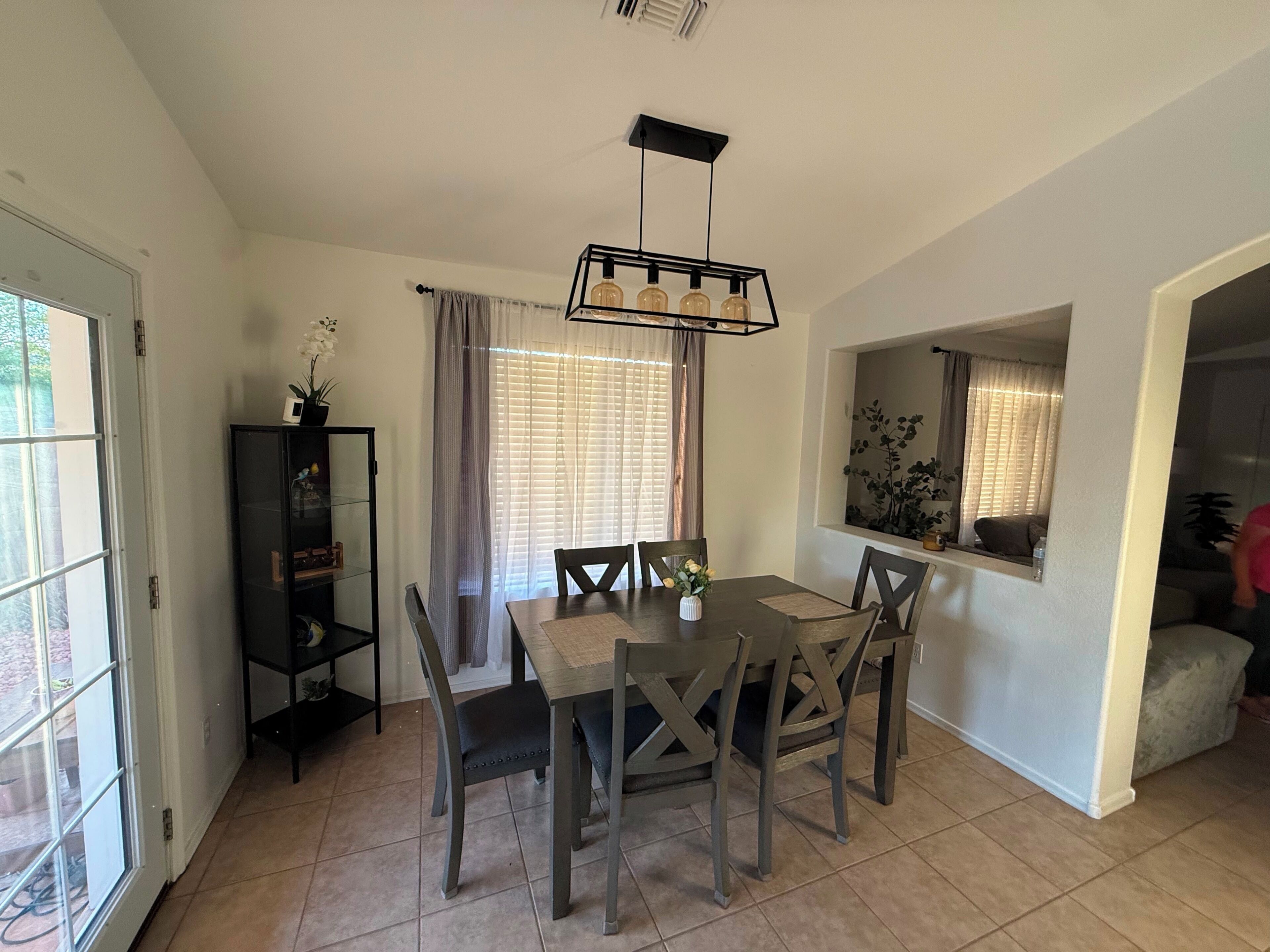 A dining area with a table and chairs, a pendant light, and a window with curtains.