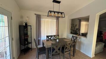 A dining area with a table and chairs, a pendant light, and a window with curtains.