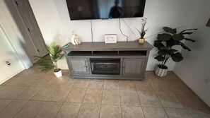 A living room with a fireplace, a television mounted on the wall, and potted plants.