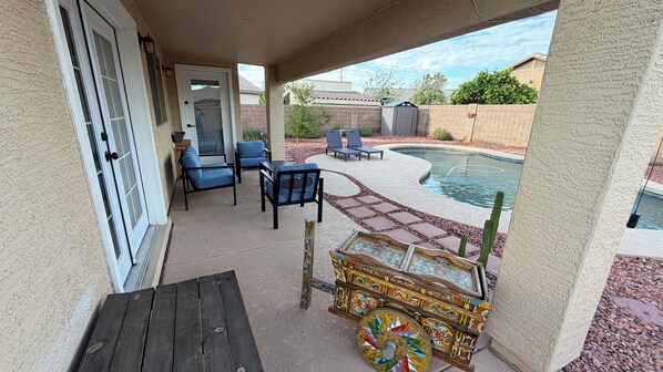 A covered patio area with a pool, outdoor furniture, and a decorative wooden chest.