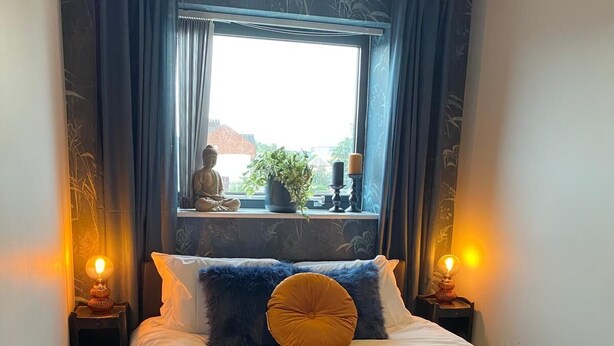 Ein Schlafzimmer mit einem Bett, zwei Nachttischlampen, einem Fenster mit Aussicht und einer Buddha-Statue auf dem Fensterbrett.