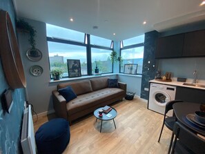 A modern living room with a sofa, coffee table, and a washing machine in the corner. - Modern 1BR Apartment near MCR Stadiums (Stretford)