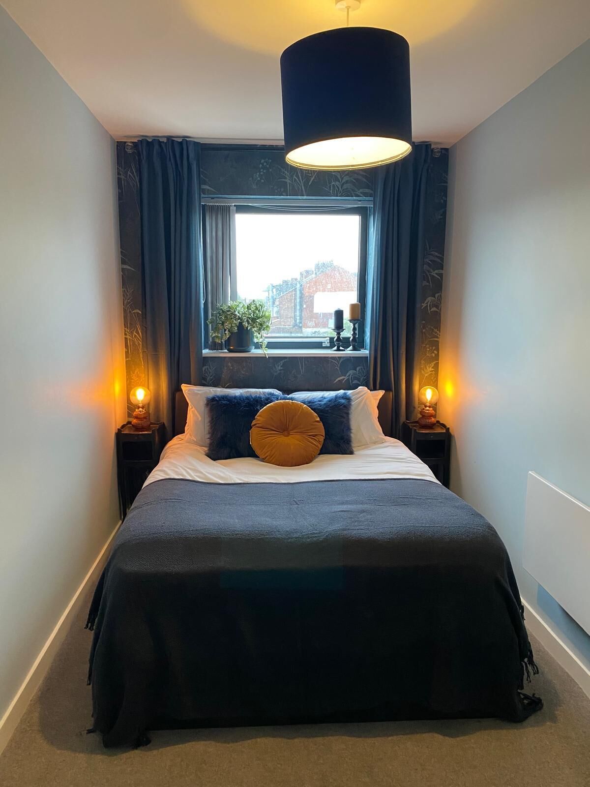 A bedroom with a bed, two bedside lamps, a window with curtains, and a hanging light fixture.