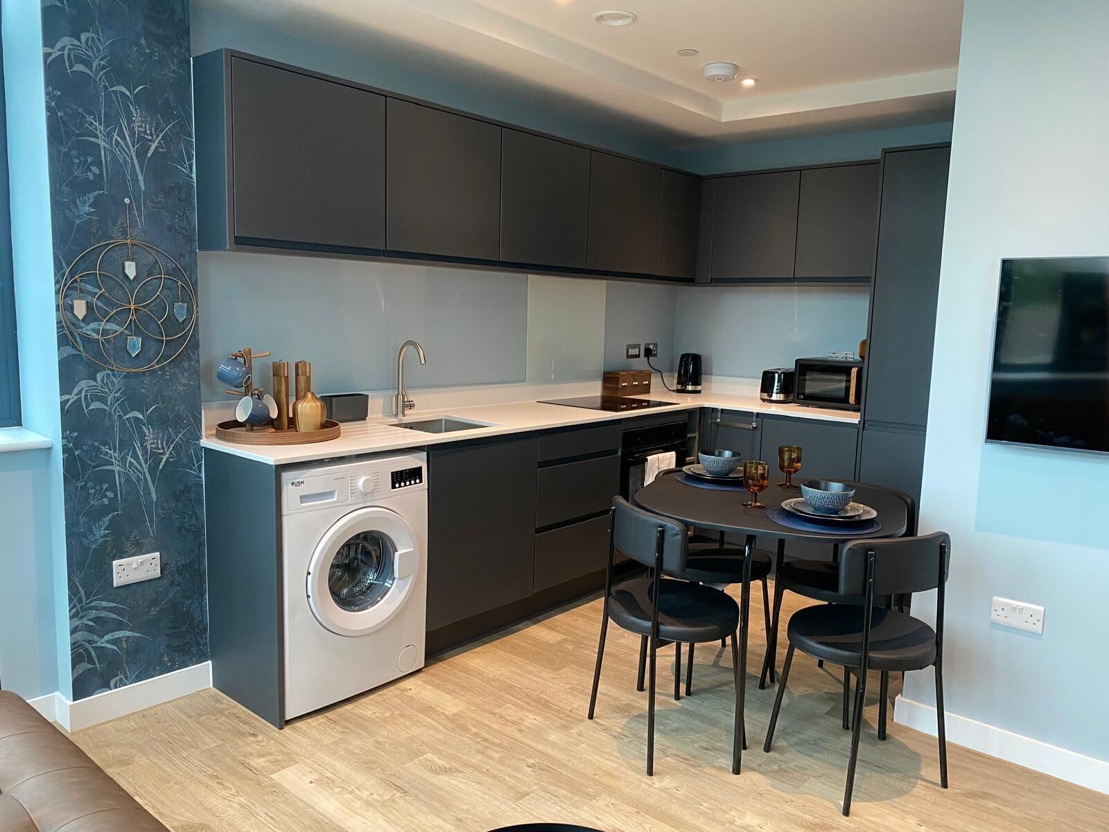 A compact kitchen with a washing machine, a dining table with chairs, and a microwave.