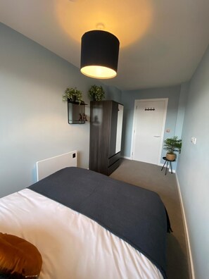 A bedroom with a bed, a wardrobe, a desk, and a door. - Modern 1BR Apartment near MCR Stadiums (Stretford)
