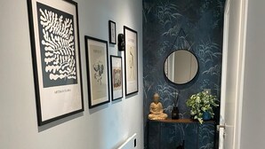 Ein Flur mit blauem Teppich, gerahmten Bildern, einer Buddha-Statue und einem Spiegel auf einer Konsole.