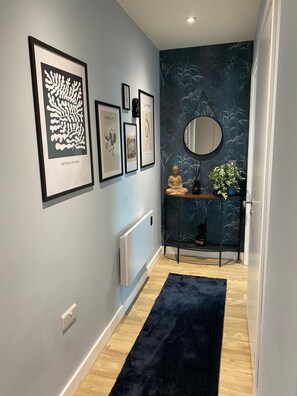 A hallway with a blue rug, framed artwork, a Buddha statue, and a mirror on a console. - Modern 1BR Apartment near MCR Stadiums (Stretford)