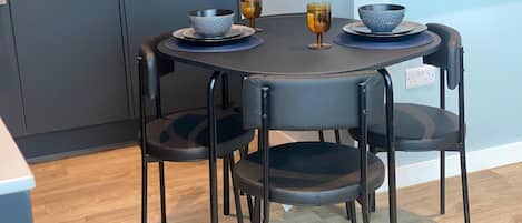 A dining area with a round table, four chairs, and a microwave in the background.