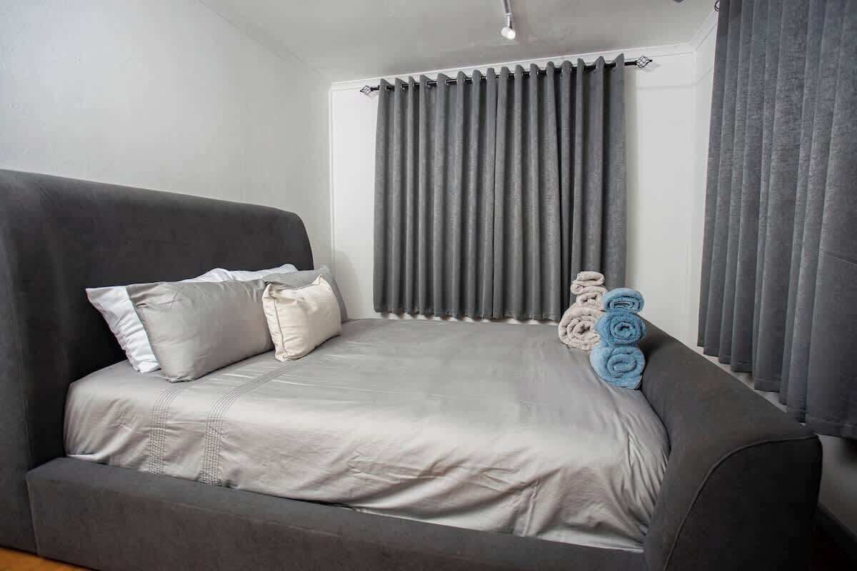 Una habitación con un sofá gris, una cama con ropa de cama gris y una ventana con cortinas grises.