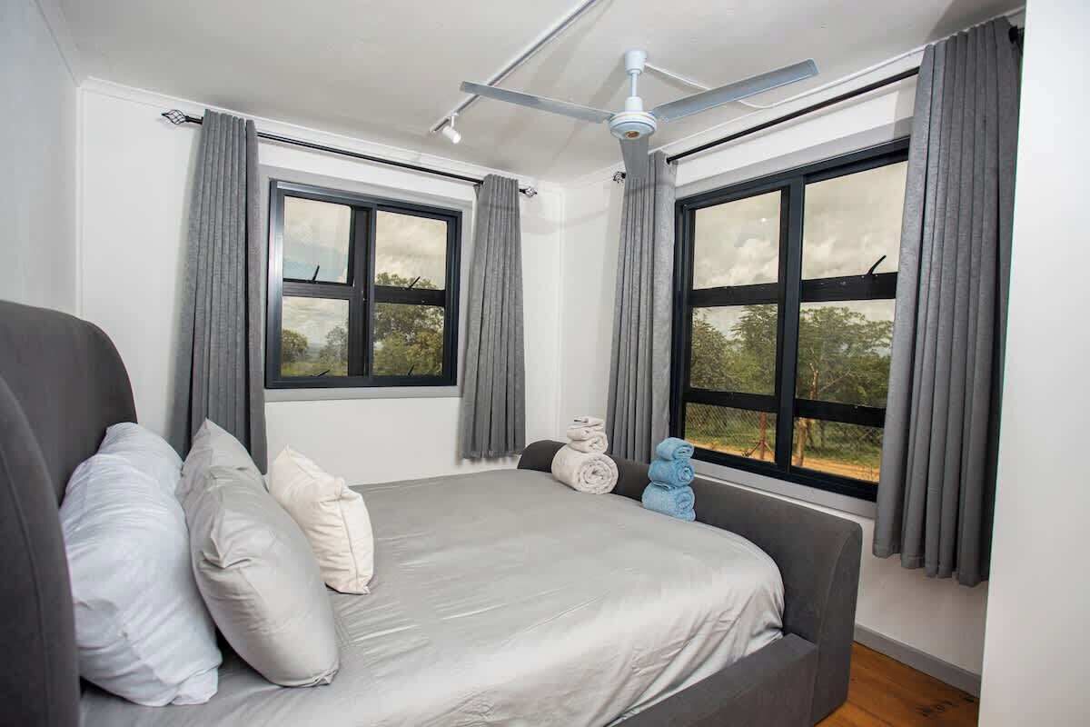 A bedroom with a bed, two windows, a ceiling fan, and a view of the outdoors.