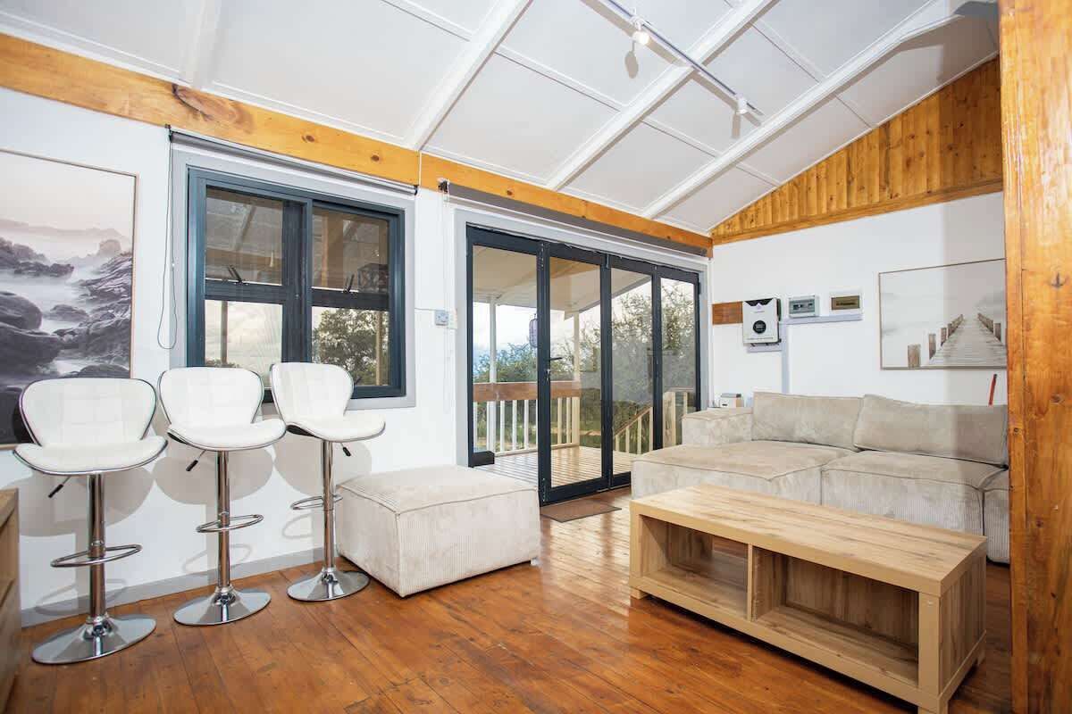 Una sala de estar moderna con piso de madera, un sofá, una mesa de centro y tres taburetes blancos.