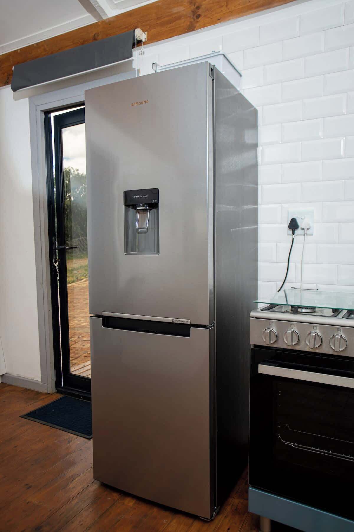 A stainless steel refrigerator with a water dispenser and a built-in oven to the right.
