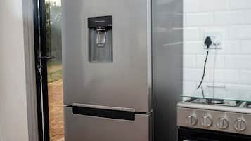 A stainless steel refrigerator with a water dispenser and a built-in oven to the right.