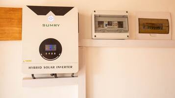 A hybrid solar inverter with a digital display, mounted on a wall above a white shelf.