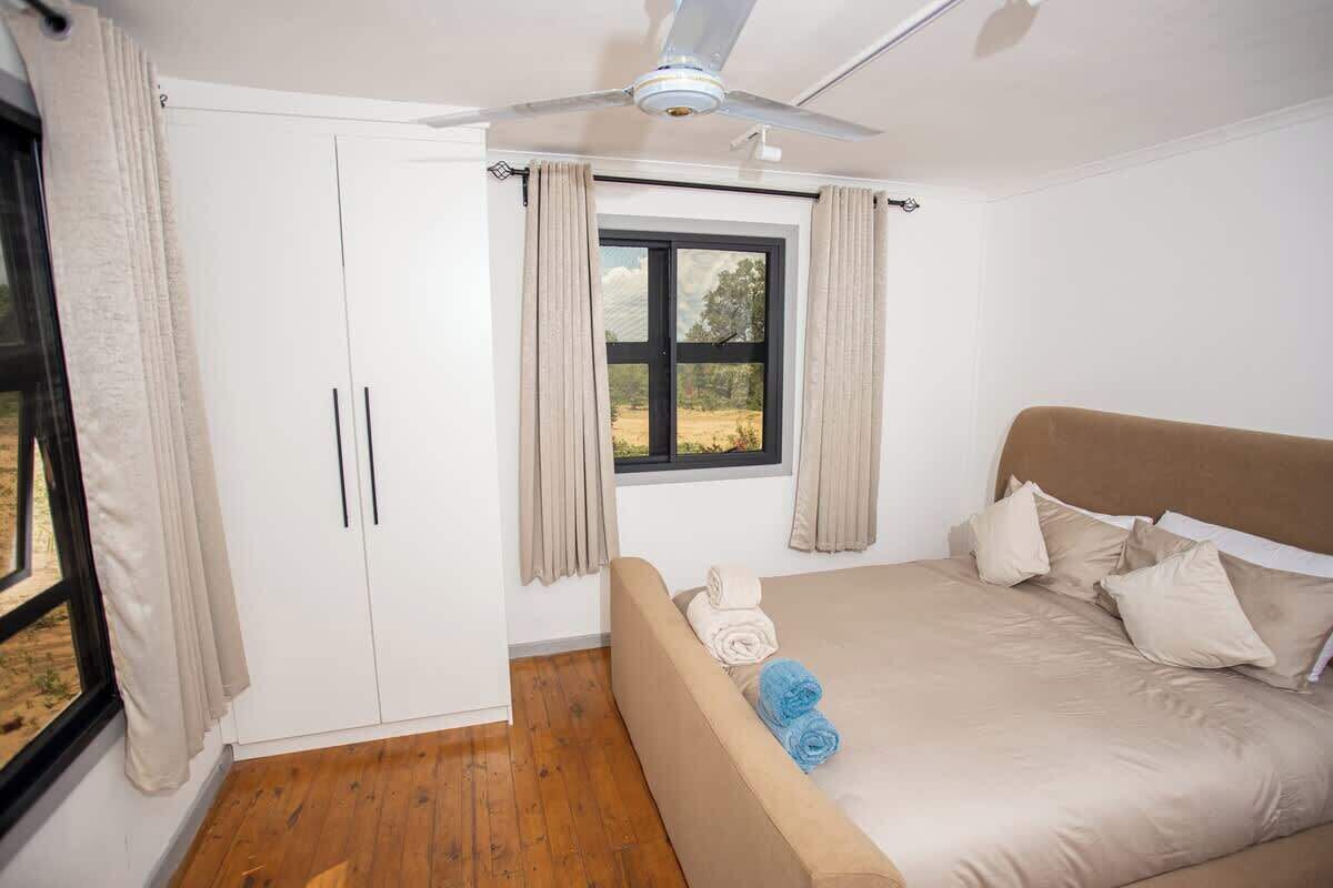A bedroom with a bed, a ceiling fan, a window with curtains, and a wardrobe.