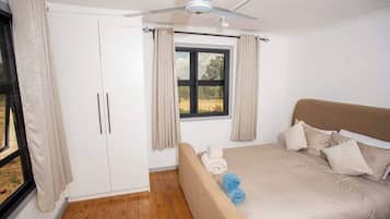 A bedroom with a bed, a ceiling fan, a window with curtains, and a wardrobe.