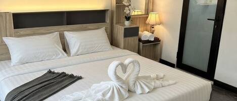 A hotel room with a large bed, a nightstand with a lamp, a mirror, and a door.