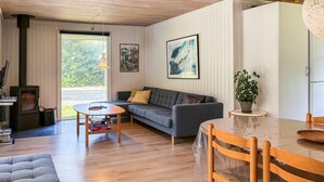 Ein gemütliches Wohnzimmer mit einer Couch, einem Couchtisch, einem Esstisch mit Stühlen, einem Kamin und einem großen Fenster.