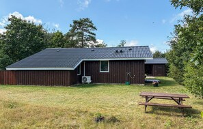 Ein hölzernes Bauernhaus mit geneigtem Dach, eine kleine angebaute Werkstatt, ein Picknicktisch und eine Rasenfläche.