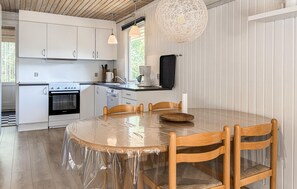 A kitchen with white cabinets, a stove, a dishwasher, and a dining area with a round table and wooden chairs. - Lovely home in Løgstør with WiFi (Løgstør)
