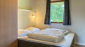 Ein Einzelbett mit weißer Bettwäsche in einem Raum mit Holzwänden und einem Fenster mit Vorhängen.