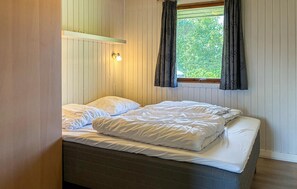 Ein Einzelbett mit weißer Bettwäsche in einem Raum mit Holzwänden und einem Fenster mit Vorhängen.