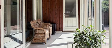 A covered outdoor area with wicker furniture and a suitcase, a door, and a potted plant.