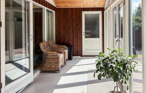 Et overdækket udendørsareal med fletningsmøbler, en kuffert, en dør og en potteplante.