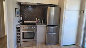 A compact kitchen with a built-in oven, a stainless steel refrigerator, and a gas stove. - Comfy Haven in the Heart of Picton (Picton)