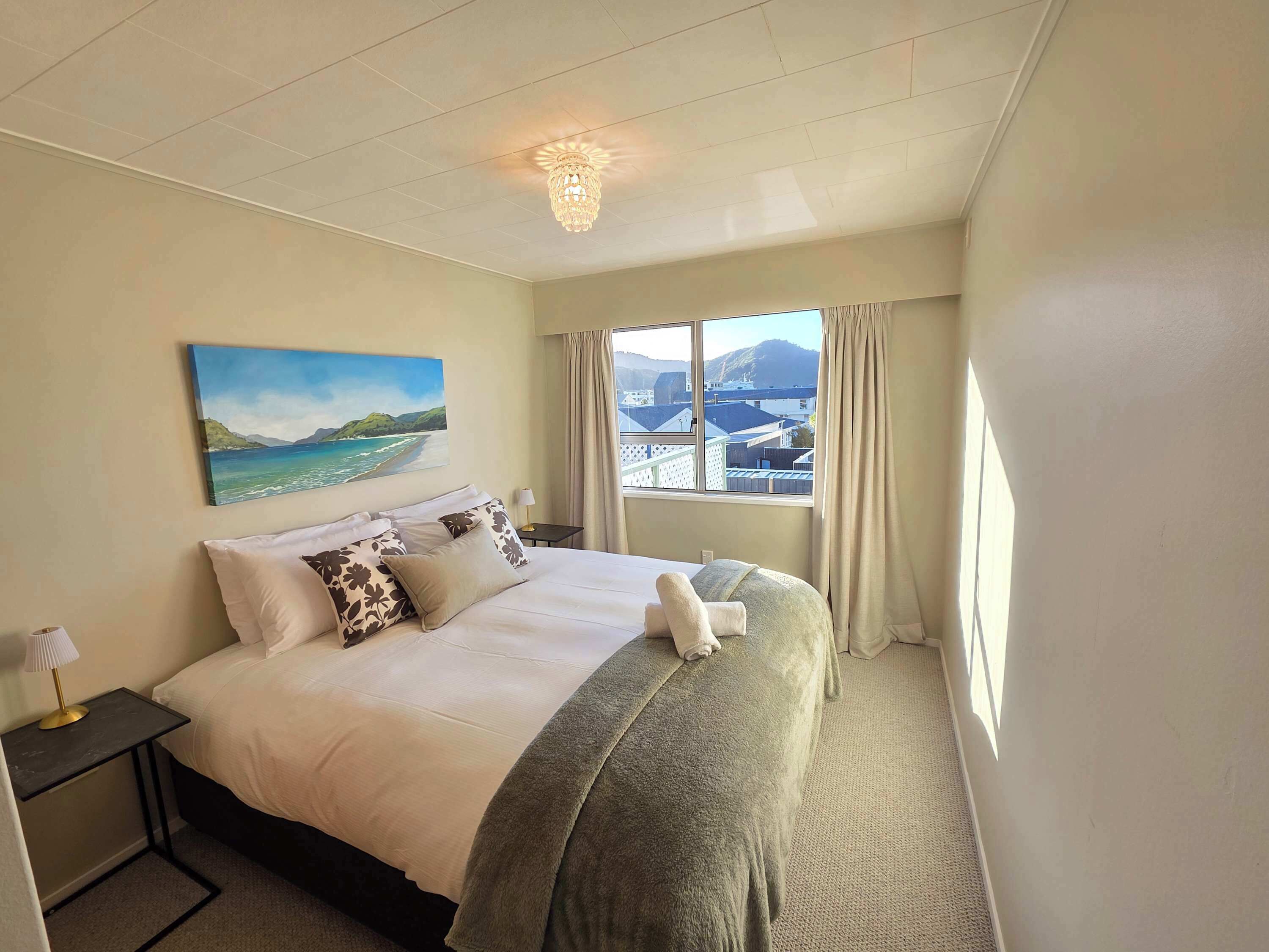 Ein Hotelzimmer mit Bett, einem Strandbild, einem fenster mit Vorhängen und einer Kristallleuchtre.