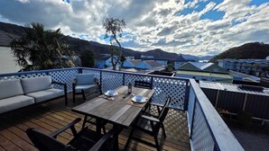 A deck with a table and chairs, a sofa, and a view of a mountainous landscape. - Comfy Haven in the Heart of Picton (Picton)