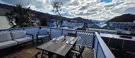 A deck with a table and chairs, a sofa, and a view of a mountainous landscape.