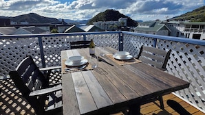 A wooden deck with a table set for two, a bottle of wine, and a bowl. - Comfy Haven in the Heart of Picton (Picton)