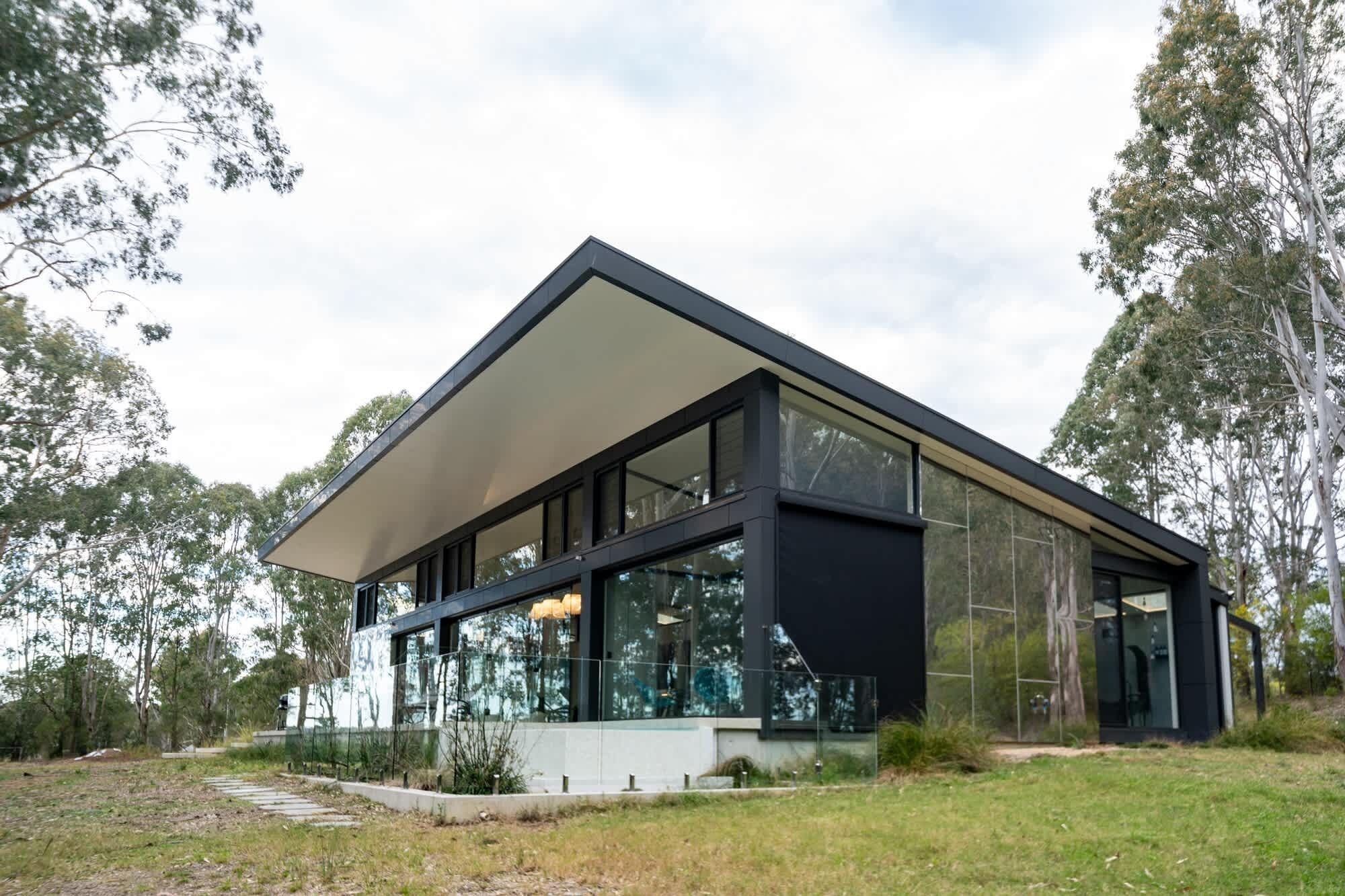 Une maison moderne à deux étages, dotée de grandes fenêtres, d’un toit plat et d’une pelouse bien entretenue.